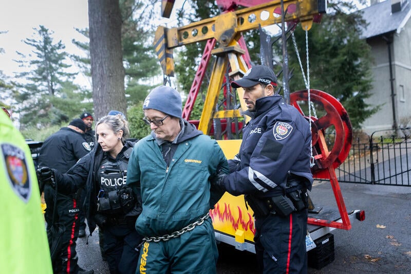 a protestor getting arrested with a replica oil pumpjack in the background