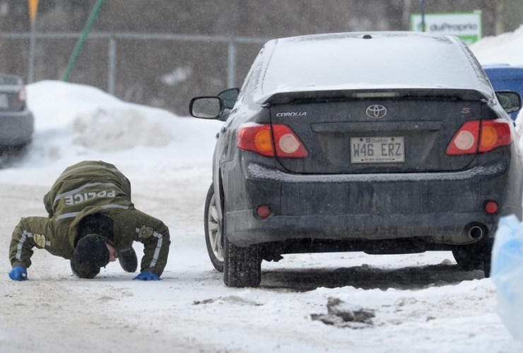 A police officer looks for evidence under a car near a Quebec City mosque on Monday January 30, 2017, where a shooting left six people dead and eight others injured Sunday. Photo by Paul Chiasson/CP.