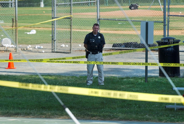 A police officer stands watch behind police tape near strewn softballs on a field in Alexandria, Va., on Wednesday, June 14, 2017, after a multiple shooting involving House Majority Whip Steve Scalise of La. 