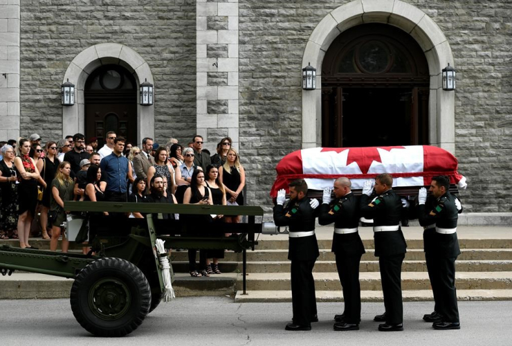 Mourners stand on the steps of the Paroisse Saint-Gregoire-de-Nazianze as the casket of Bombardier Patrick Labrie is carried inside on July 6, 2019. File photo by The Canadian Press