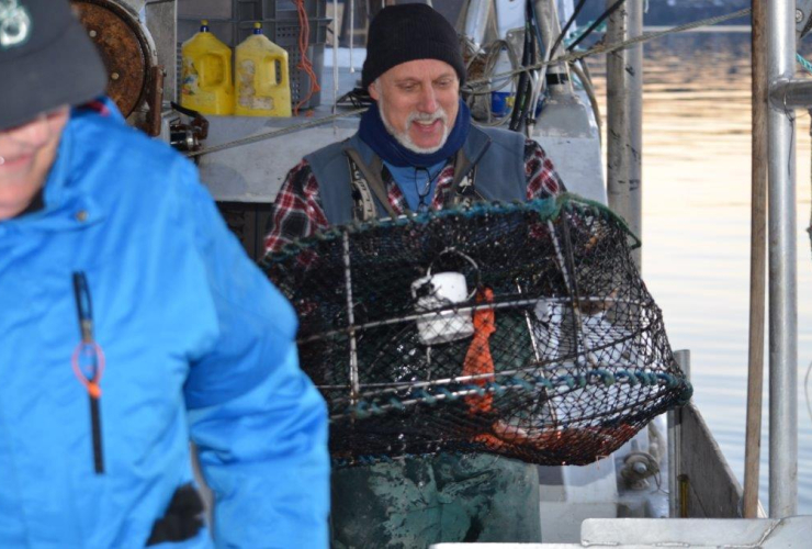 Guy Johnson carrying a prawn trap on a boat deck.