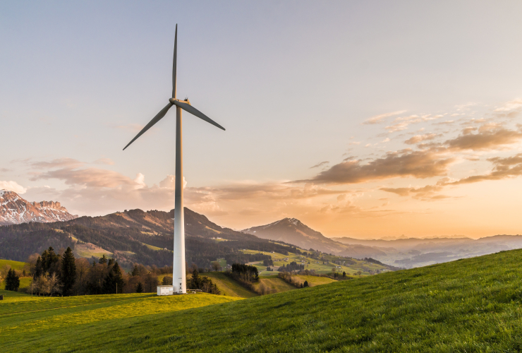 A white windmill on a grassy hill with jagged mountains in the backdrop.