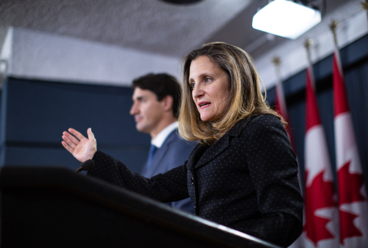 A woman standing at a podium gestures with one arm, pointing forwards as she speaks