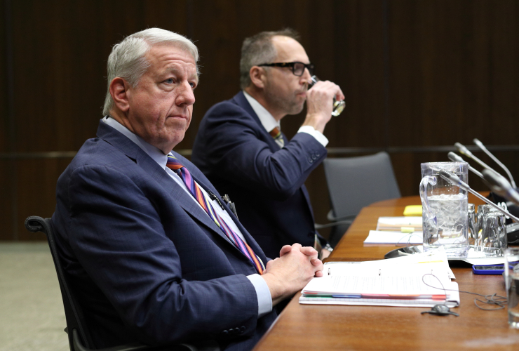 a man in a suit sits at a wooden table before a committee meeting begins