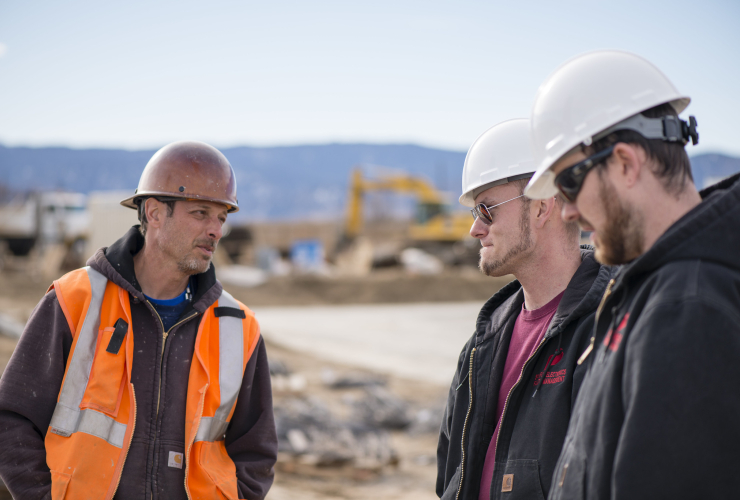 three construction workers wearing hard hats and sunglasses talking