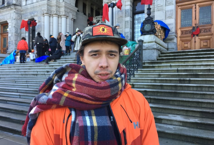 a man in an orange jacket stands in front of the Victoria legislature