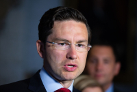 A bespectacled man wearing a suit is photographed mid-sentence