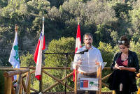 A man stands on a wooden platform looking out ona  forest, with a translator to his left