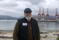 A bearded man stands in front of a small shipping terminal in Vancouver