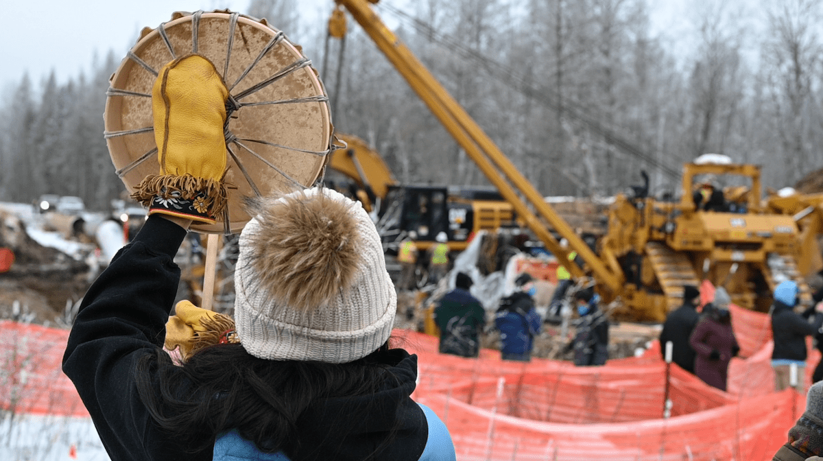 A person in a toque holds a drum next to a construction site