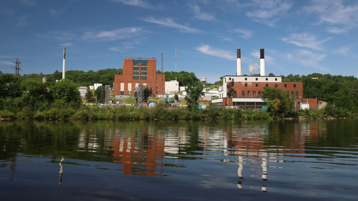 Brick buyildings and smoke stacks of the Chalk River nuclear laboratory are visible from the river on a bright, sunny day