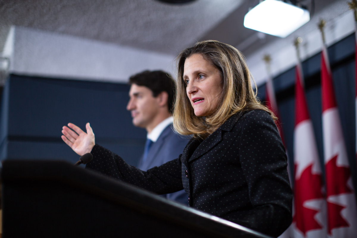 A woman standing at a podium gestures with one arm, pointing forwards as she speaks