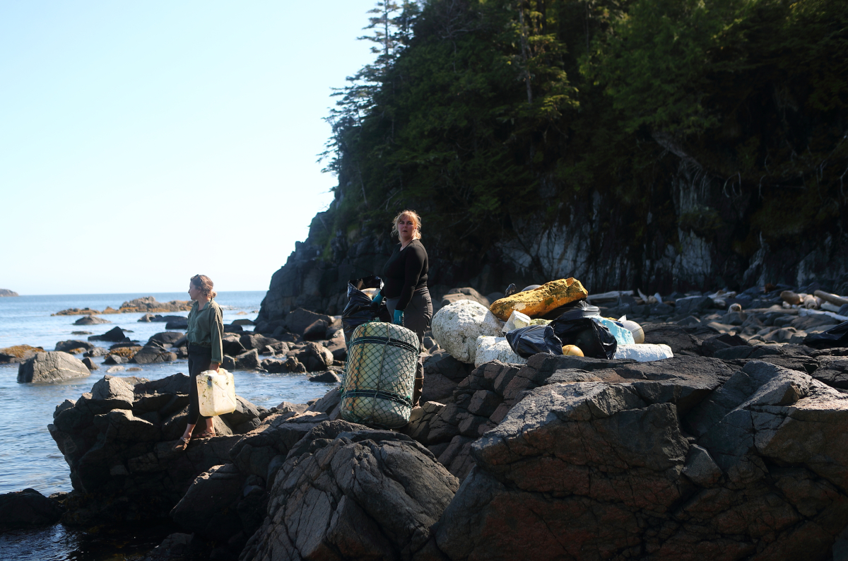 Two people stand with a pile of garbage at a rocky point, reparing to load it into a zodiac