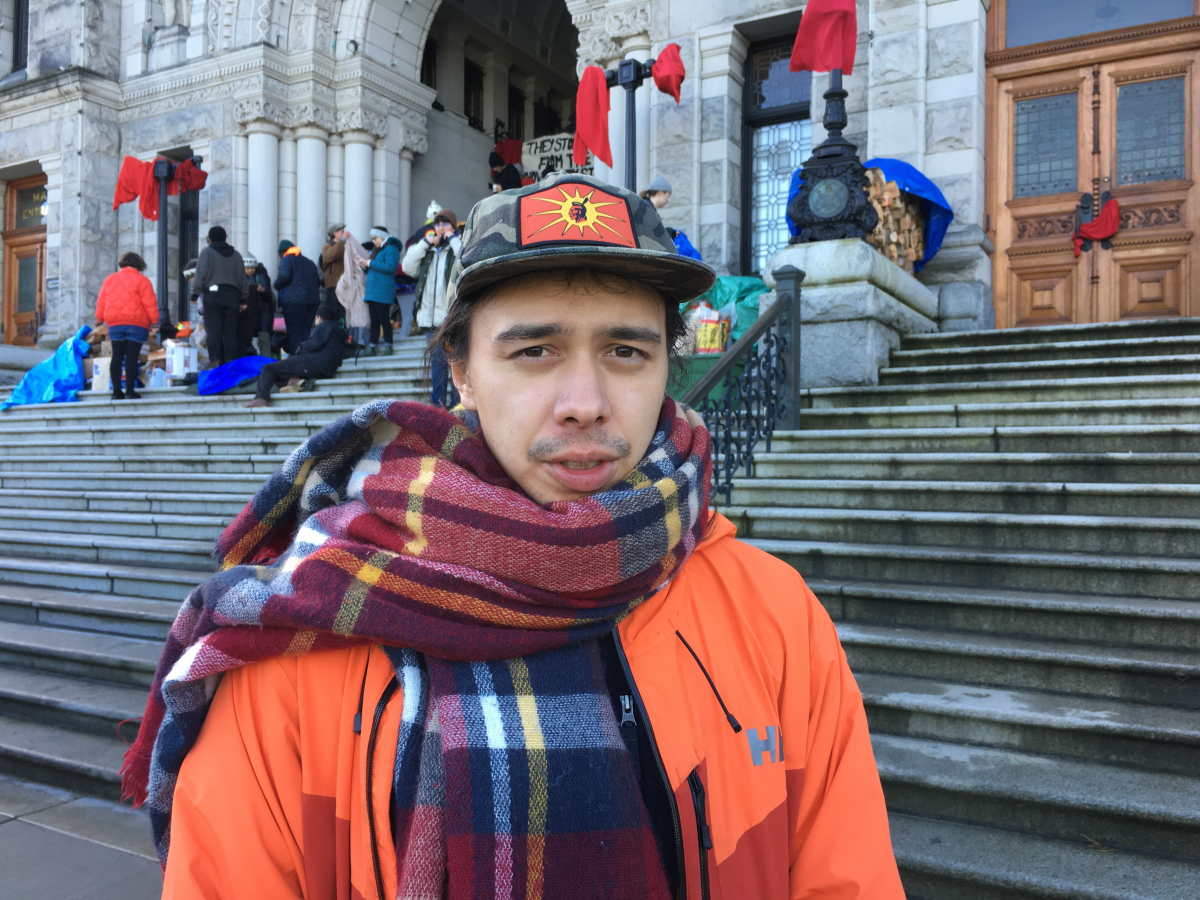 a man in an orange jacket stands in front of the Victoria legislature