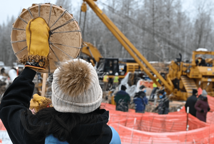 A person in a toque holds a drum next to a construction site